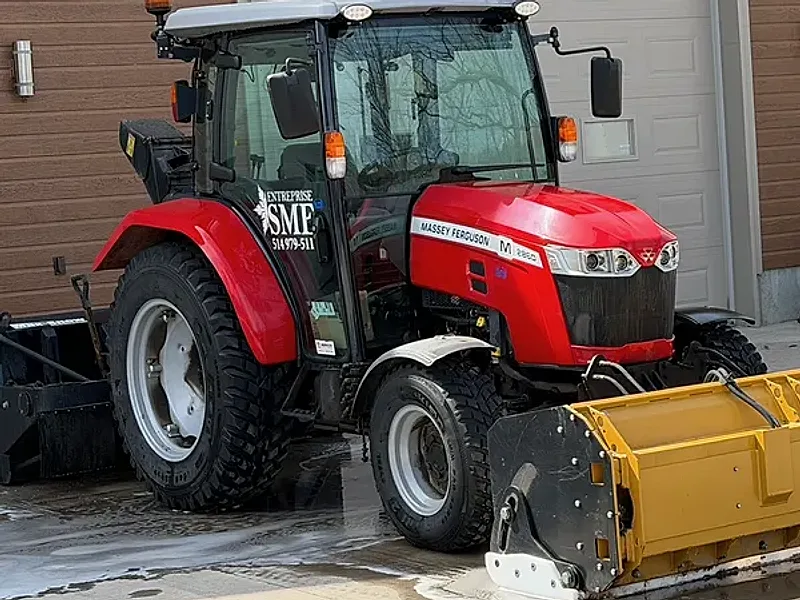 Tracteur Massey Ferguson rouge lettré Entreprise SME, gratte à neige jaune à l'avant, devant le garage