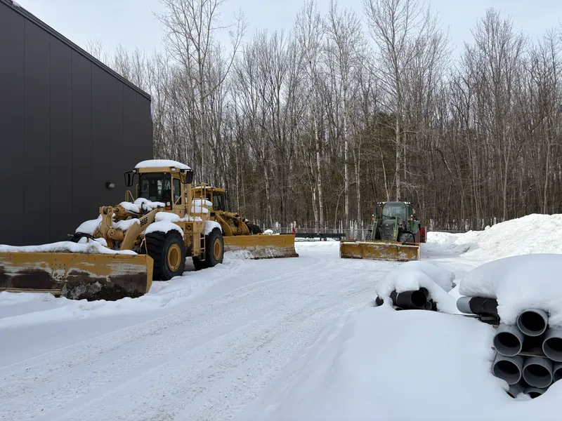 La flotte commerciale de l'Entreprise SME dans la neige : deux chargeuses à lame large et un tracteur John Deere avec lame, devant un bâtiment industriel