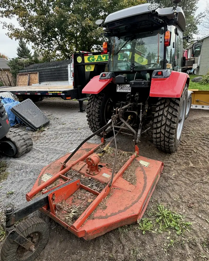 Tracteur rouge de l'Entreprise SME attelé à un gyrobroyeur, prêt pour le débroussaillage