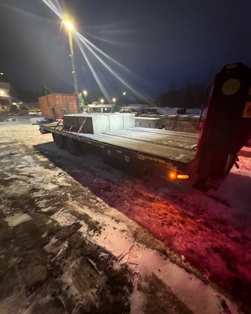 Remorque à col de cygne chargée de blocs de béton, feux de gabarit allumés, le soir sous l'éclairage d'un chantier enneigé